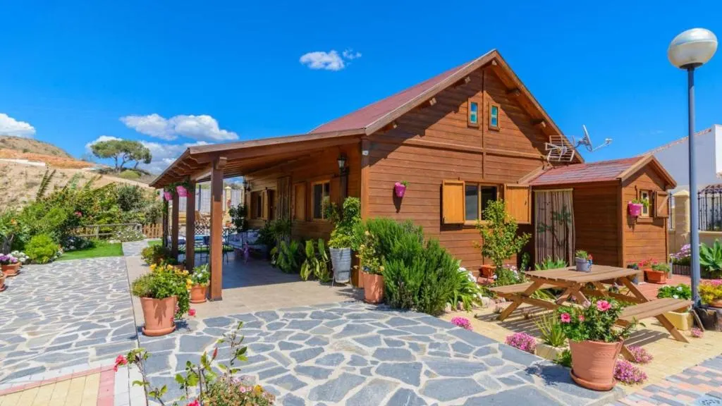 Fachada de madera de Casa Alegría, con el porche de entrada y el jardín con macetas