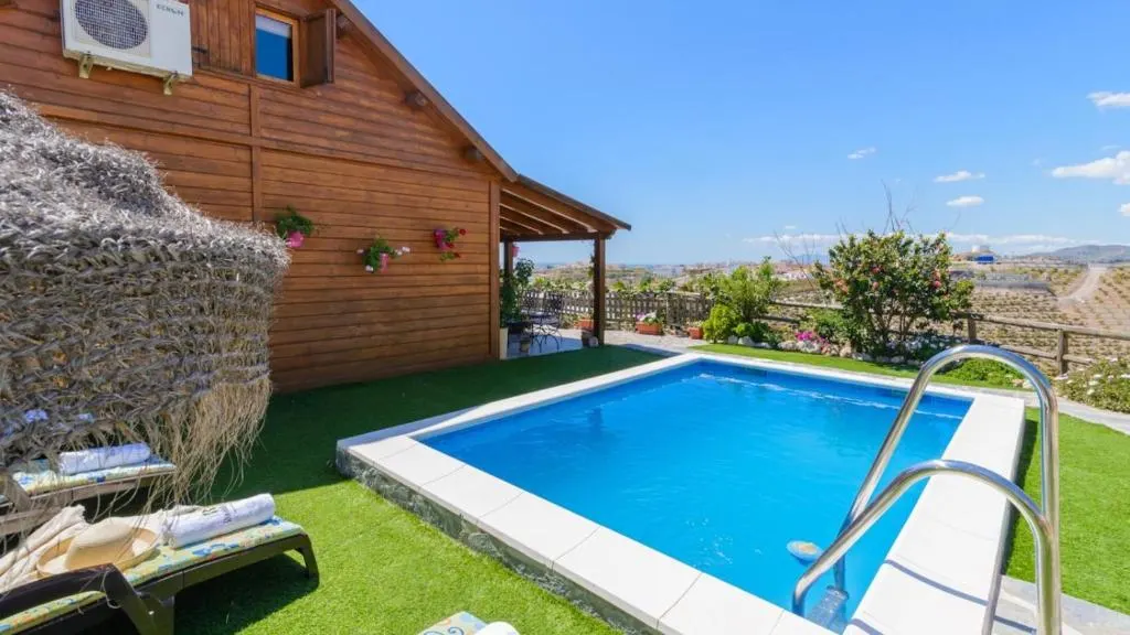 Piscina privada y jardín de Casa Alegría en Almayate Alto, con la casa de madera y vistas al valle al fondo