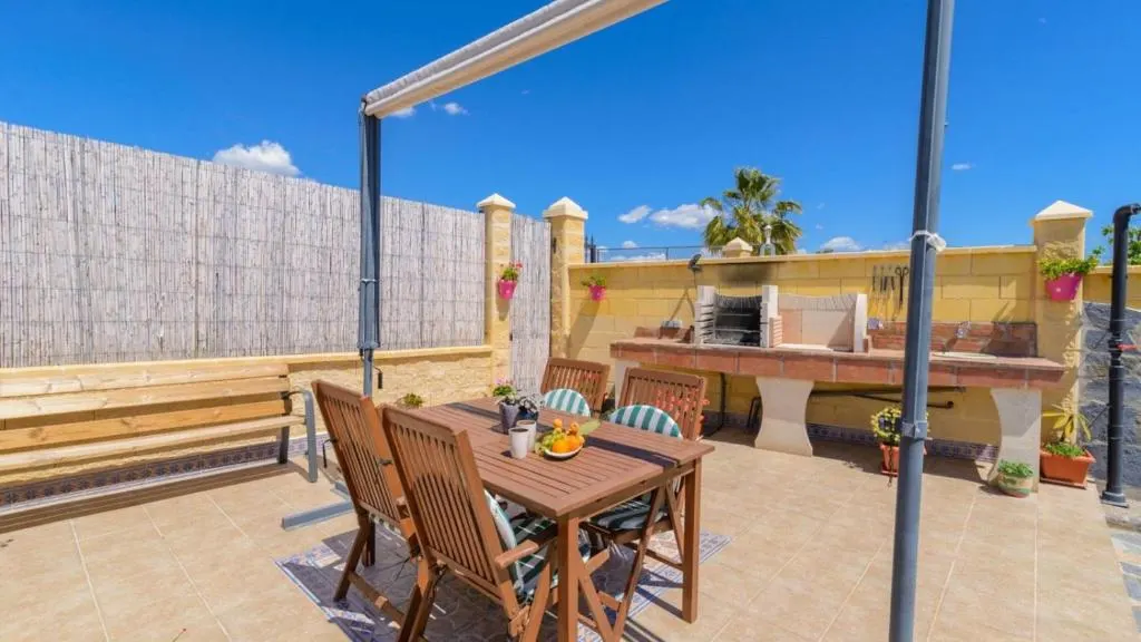 Terraza con barbacoa de obra y mesa para comer al aire libre en Casa Alegría