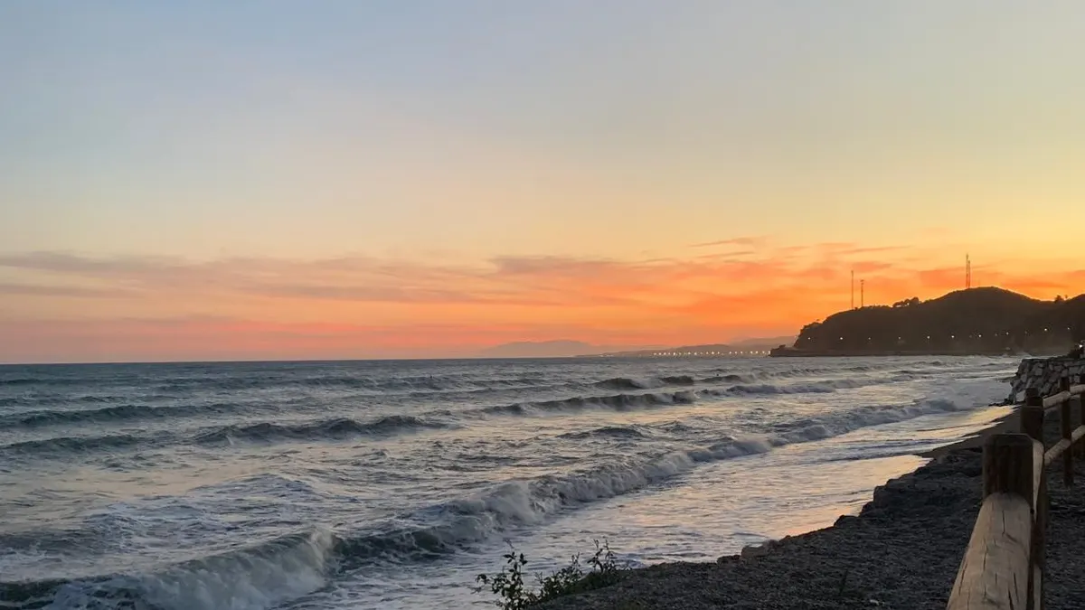 Atardecer en la playa de Lagos (Vélez-Málaga), con olas rompiendo en la orilla y la costa al fondo